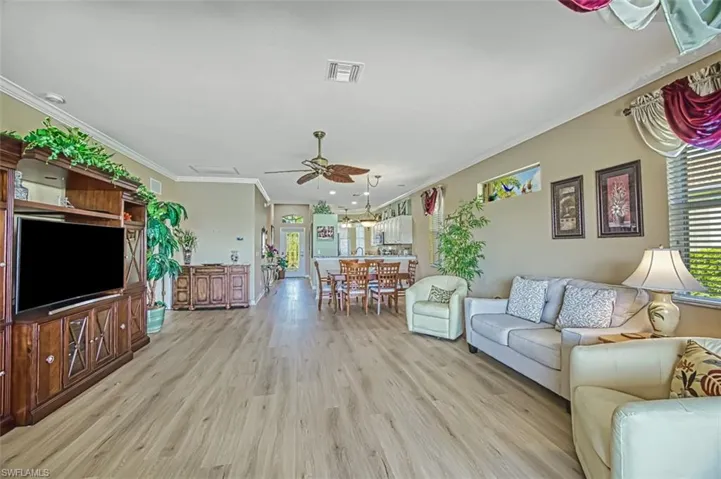 Living room with light wood-type flooring, ceiling fan, and crown molding