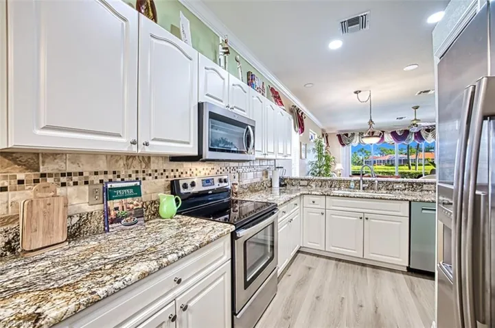 Kitchen with light hardwood / wood-style flooring, appliances with stainless steel finishes, crown molding, sink, and white cabinetry
