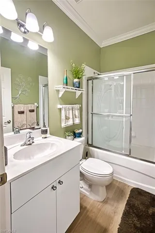 Full bathroom featuring crown molding, hardwood / wood-style floors, toilet, shower / bath combination with glass door, and vanity