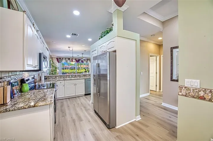 Kitchen with white cabinets, light wood-type flooring, stainless steel appliances, dark stone counters, and ornamental molding
