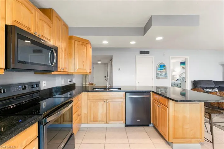 Kitchen with appliances with stainless steel finishes, a peninsula, light tile patterned floors, dark stone countertops, and recessed lighting