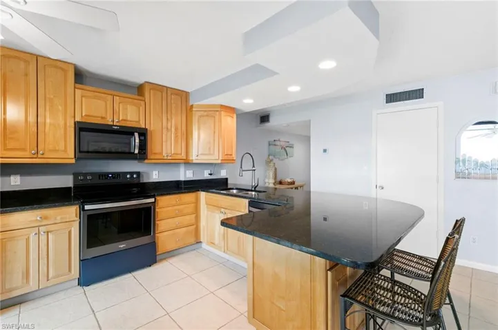 Kitchen with stainless steel range with electric stovetop, light tile patterned flooring, black microwave, dark stone counters, and recessed lighting