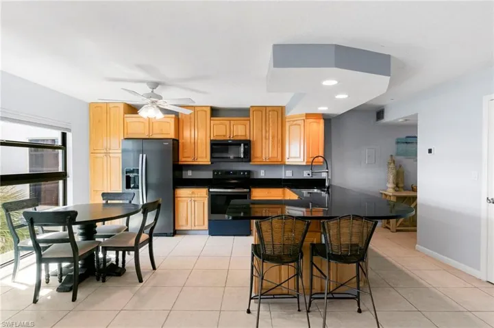 Kitchen with electric range oven, fridge with ice dispenser, a peninsula, black microwave, and recessed lighting