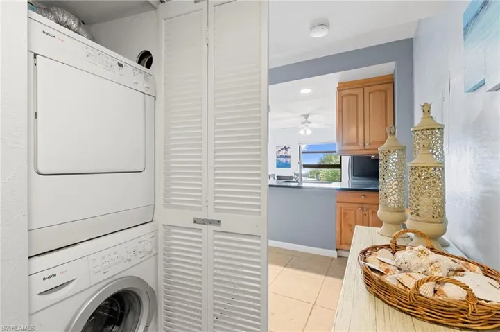 Laundry area featuring light tile patterned floors, stacked washer / dryer, and a ceiling fan