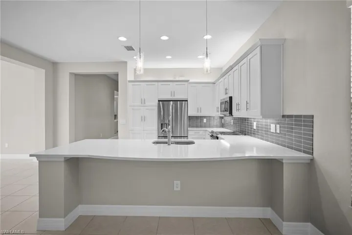 Kitchen with appliances with stainless steel finishes, backsplash, light tile patterned floors, a breakfast bar, and light stone countertops