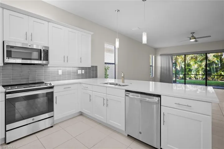 Kitchen with stainless steel appliances, backsplash, a peninsula, light tile patterned floors, and white cabinetry