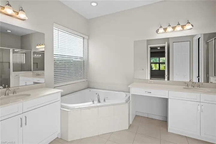 Bathroom featuring a stall shower, two vanities, a bath, and light tile patterned floors