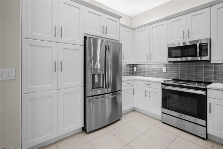Kitchen featuring appliances with stainless steel finishes, backsplash, light tile patterned floors, white cabinetry, and light stone countertops