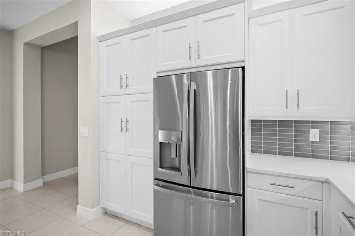 Kitchen featuring stainless steel refrigerator with ice dispenser, white cabinets, light tile patterned floors, tasteful backsplash, and light stone countertops