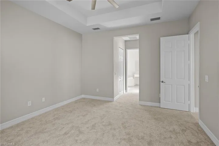 Unfurnished bedroom featuring light carpet, a tray ceiling, connected bathroom, and ceiling fan