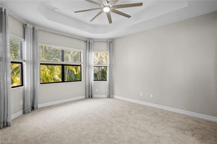Unfurnished room with a tray ceiling, light colored carpet, and a ceiling fan
