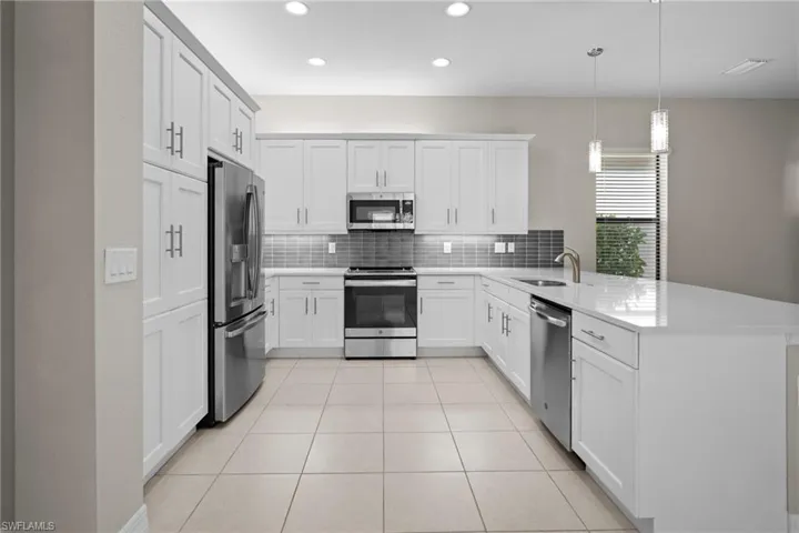 Kitchen with stainless steel appliances, backsplash, a peninsula, decorative light fixtures, and light tile patterned flooring