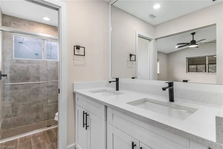 Bathroom featuring double vanity, a stall shower, wood finish floors, and a ceiling fan