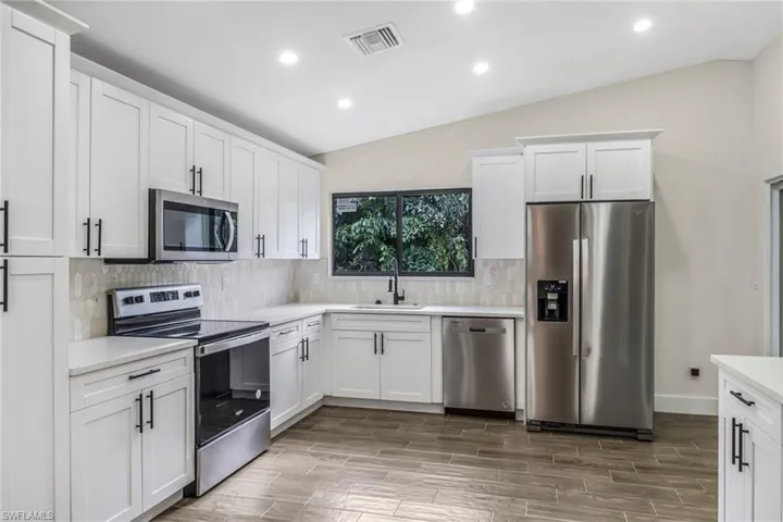 Kitchen with lofted ceiling, stainless steel appliances, white cabinets, recessed lighting, and backsplash