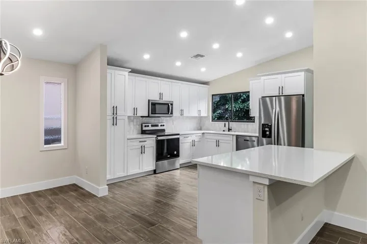 Kitchen featuring wood finish floors, stainless steel appliances, white cabinets, decorative backsplash, and recessed lighting