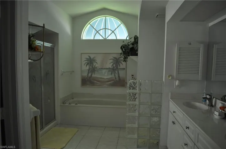 Full bath featuring vanity, a bath, a shower stall, light tile patterned floors, and vaulted ceiling