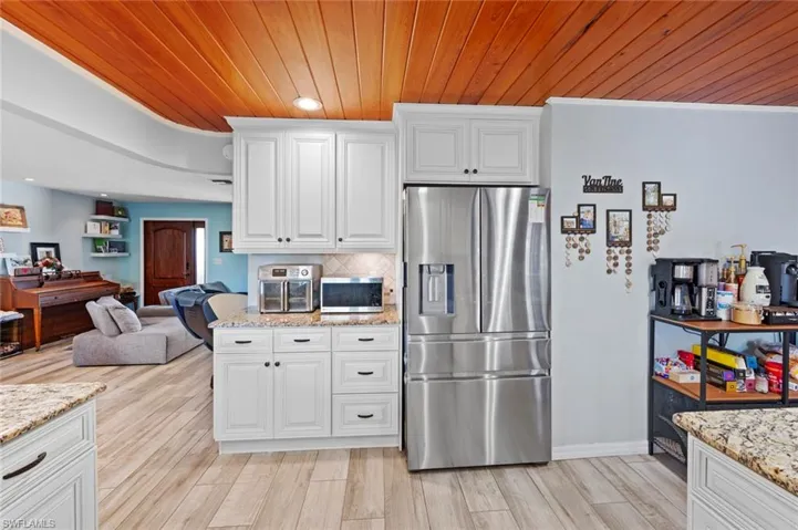 Kitchen featuring open floor plan, appliances with stainless steel finishes, wood ceiling, light stone countertops, and light wood-style flooring
