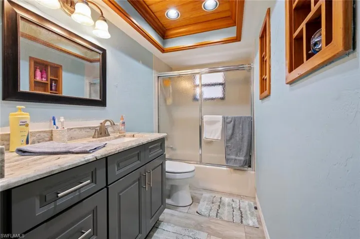 Full bath featuring combined bath / shower with glass door, toilet, crown molding, a tray ceiling, and vanity