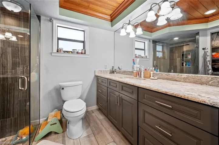 Bathroom with a shower stall, a tray ceiling, wooden ceiling, and toilet
