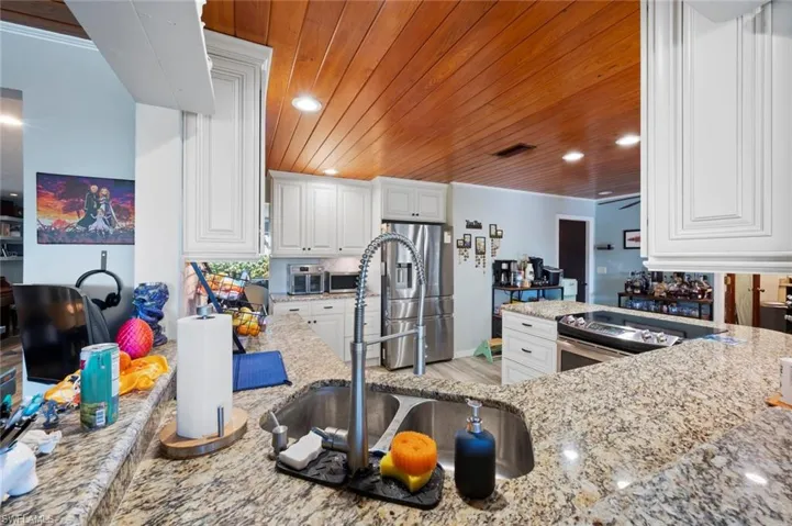 Kitchen with white cabinets, recessed lighting, wood ceiling, light stone counters, and stainless steel appliances