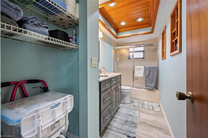 Full bathroom featuring baseboards, bath / shower combo with glass door, a tray ceiling, recessed lighting, and vanity