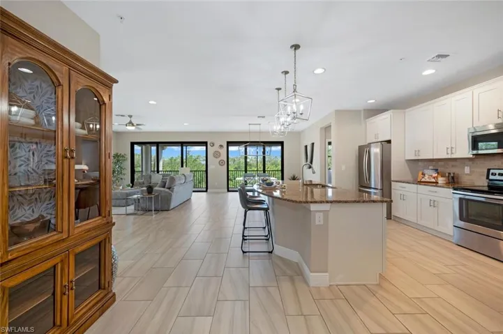 Kitchen with stainless steel appliances, decorative light fixtures, dark stone countertops, white cabinets, and a kitchen island with sink