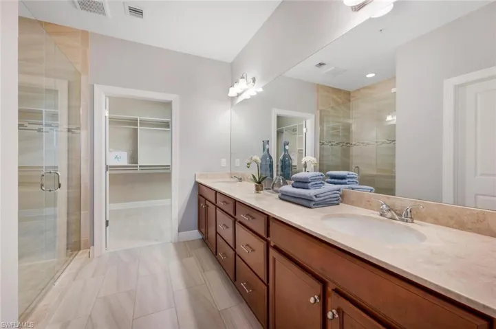 Bathroom featuring vanity with extensive cabinet space, dual sinks, tile floors, and a shower