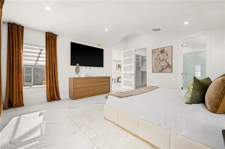 Bedroom featuring connected bathroom, a spacious closet, light marble finish flooring, lofted ceiling, and recessed lighting