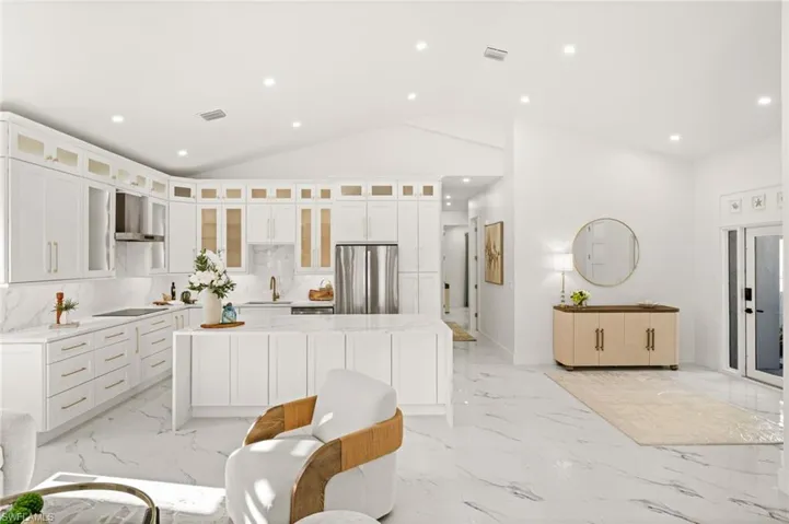 Kitchen featuring light stone countertops, a kitchen island, freestanding refrigerator, white cabinets, and glass insert cabinets