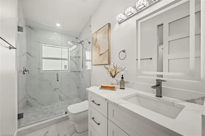 Full bath featuring vanity, a marble finish shower, light marble finish flooring, and recessed lighting