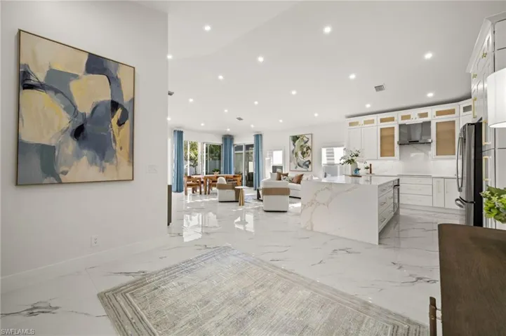 Kitchen featuring glass fronted cabinets, white cabinetry, light stone counters, open floor plan, and recessed lighting