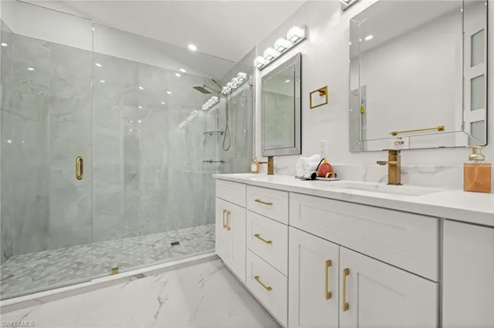 Bathroom featuring double vanity, a marble finish shower, light marble finish flooring, and recessed lighting