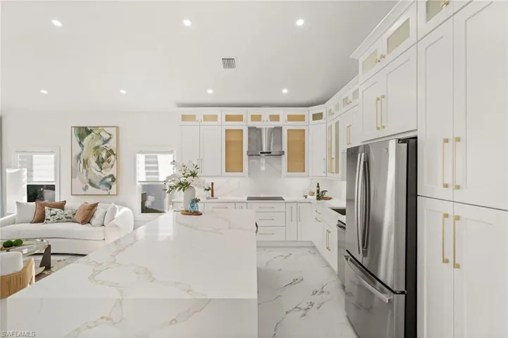 Kitchen with glass fronted cabinets, white cabinets, light stone counters, stainless steel appliances, and recessed lighting