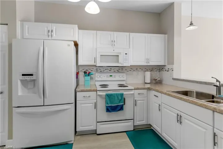 Kitchen with white cabinetry, white appliances and decorative light fixtures