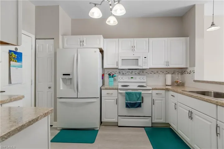 Kitchen featuring tasteful backsplash, white cabinets, hanging light fixtures, white appliances, and light wood-type flooring
