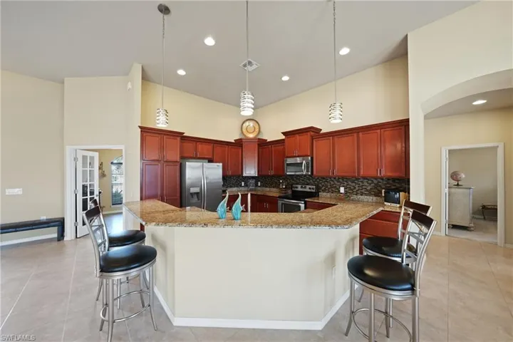 Kitchen featuring a towering ceiling, an island with sink, appliances with stainless steel finishes, decorative light fixtures, and a kitchen bar