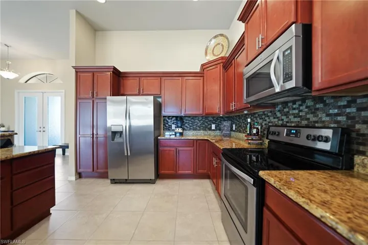Kitchen featuring light stone countertops, appliances with stainless steel finishes, french doors, light tile patterned floors, and decorative light fixtures