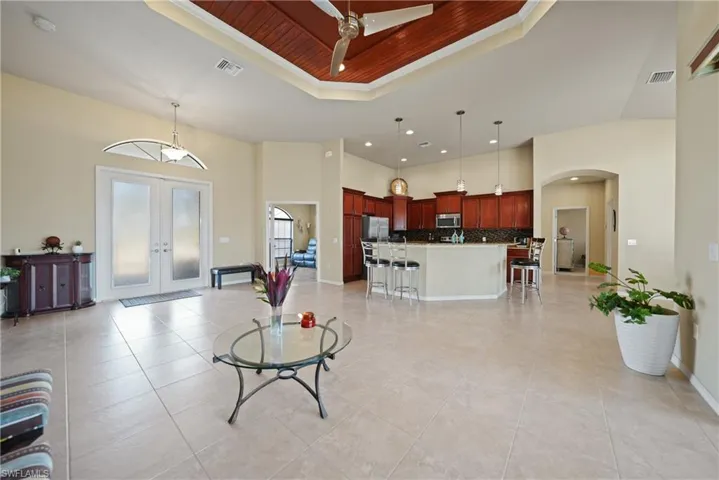 Living room featuring french doors, wood ceiling, a tray ceiling, ceiling fan, and a high ceiling