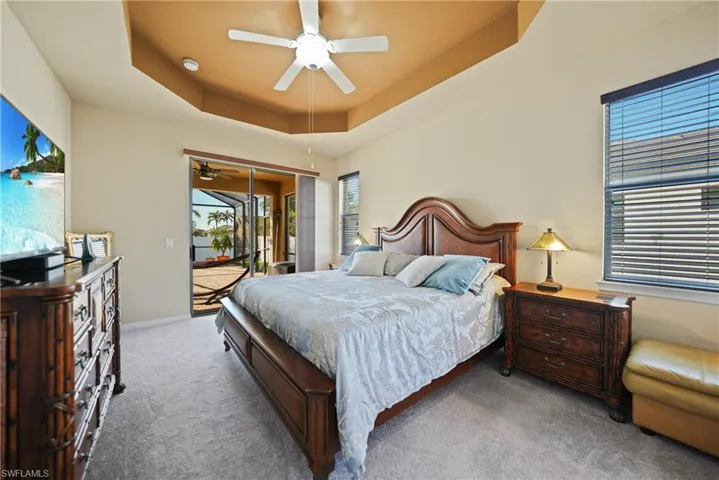 Carpeted bedroom with access to outside, a raised ceiling, and ceiling fan