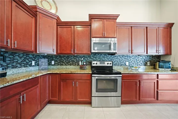 Kitchen featuring appliances with stainless steel finishes, backsplash, light stone counters, and light tile patterned flooring
