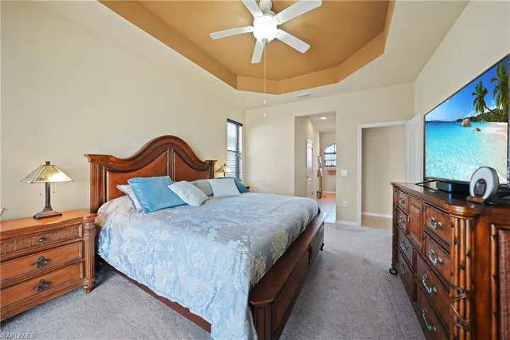 Bedroom featuring carpet floors, a tray ceiling, ceiling fan, and connected bathroom
