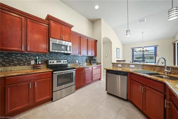 Kitchen with sink, lofted ceiling, hanging light fixtures, and appliances with stainless steel finishes
