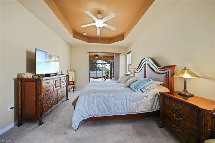 Bedroom featuring access to outside, light colored carpet, ceiling fan, and a tray ceiling