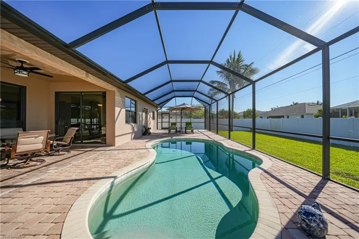 View of pool featuring glass enclosure, ceiling fan, a patio area, and a lawn