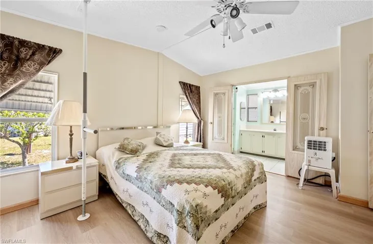 Bedroom featuring visible vents, ensuite bathroom, a textured ceiling, light wood-style floors, and lofted ceiling