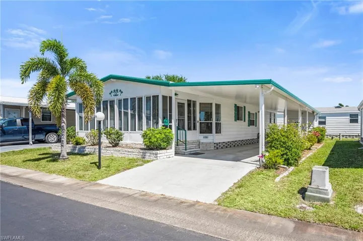 Manufactured / mobile home with a carport, concrete driveway, a front yard, and a sunroom