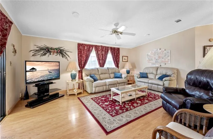 Living area with visible vents, a textured ceiling, wood finished floors, and a ceiling fan