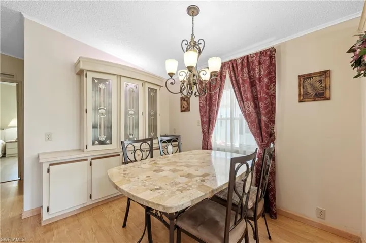 Dining room featuring an inviting chandelier, baseboards, light wood finished floors, and a textured ceiling
