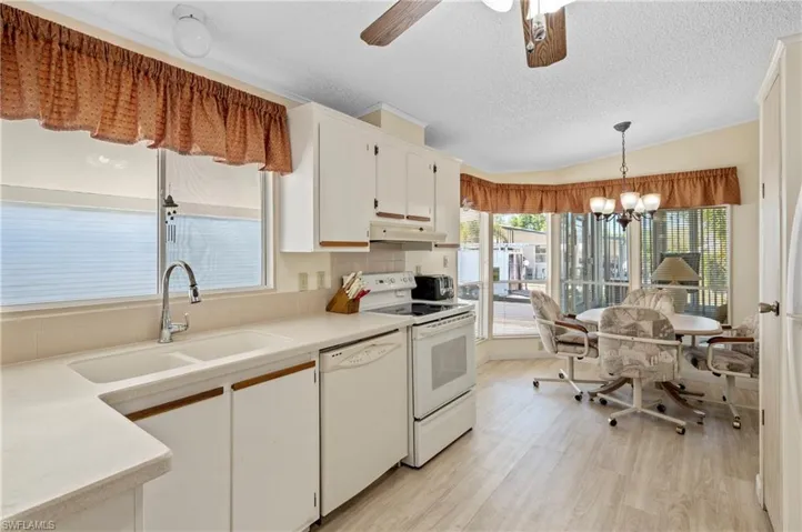 Kitchen with a sink, under cabinet range hood, white cabinetry, white appliances, and light wood-style floors