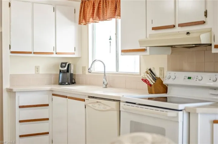 Kitchen featuring backsplash, under cabinet range hood, white appliances, white cabinetry, and a sink